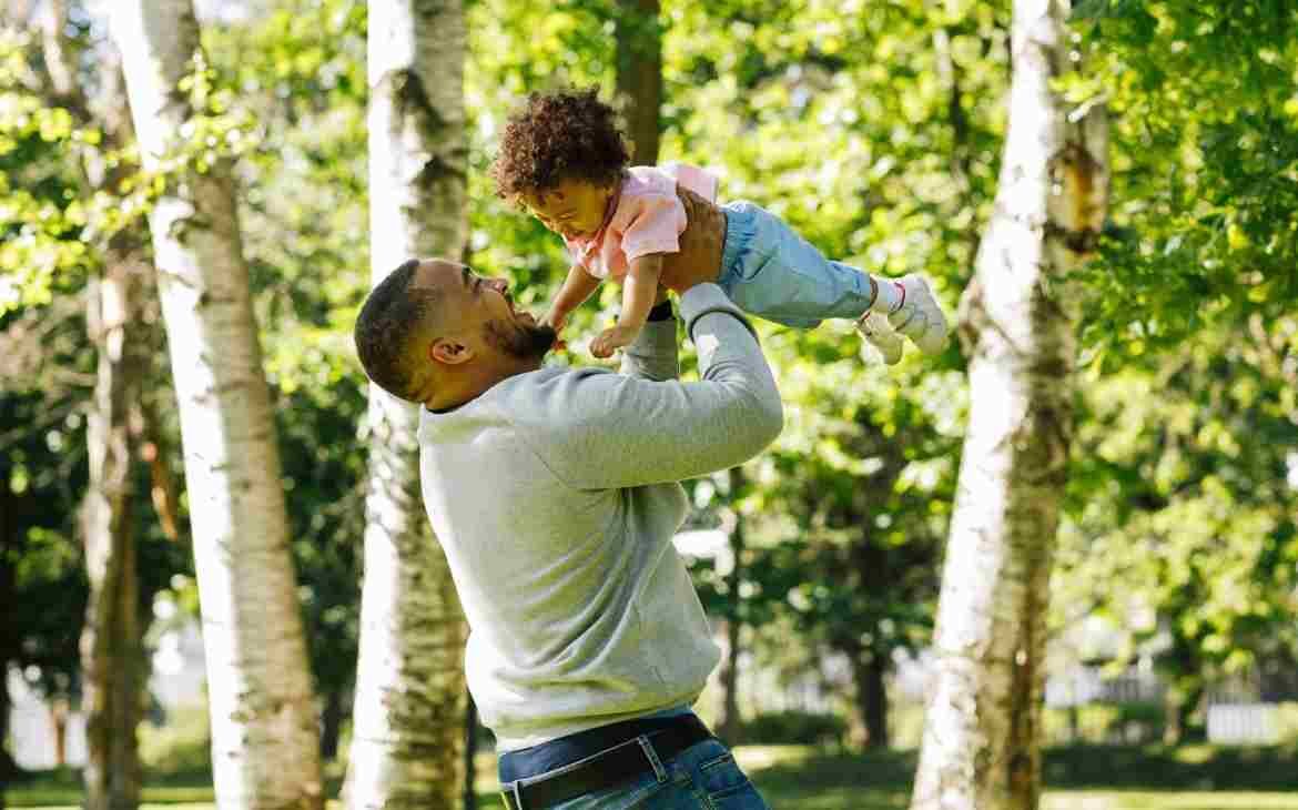 Criança em contato com a natureza. Pai segurando filha no ar no meio de árvores