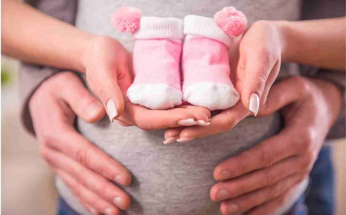 Chegada de um bebê: Mãe grávida segurando sapatinho de bebê com a mão do pai do bebê em sua barriga