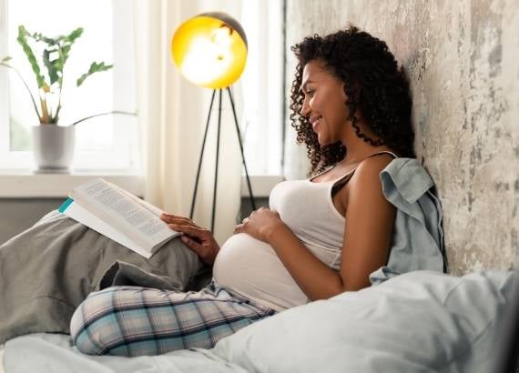 Leitura para bebês na barriga. Mãe grávida feliz lendo um livro na cama