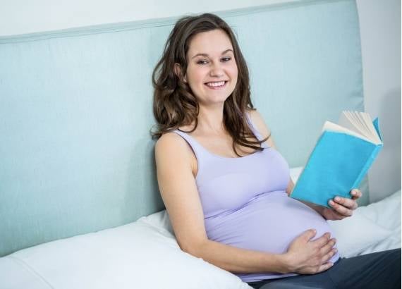 Leitura para bebês na barriga. Mãe grávida sorrindo lendo um livro