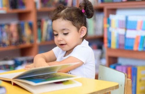 O que é formação leitora: menina sentada em uma mesa de madeira pequena enquanto folheia um livro