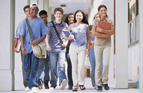 Grupo de adolescentes compostos de sete pessoas de diferentes etnias andando por um corredor de uma instituição escolar