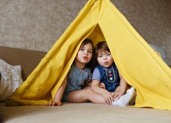 atividades para crianças 4 anos Duas crianças brincando de cabana com um cobertor dentro de casa
