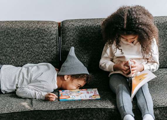 Duas crianças em um sofá, um menino deitado de bruços e uma menina folheando um livro. - Como ensinar a ler 8 dicas fáceis e práticas 