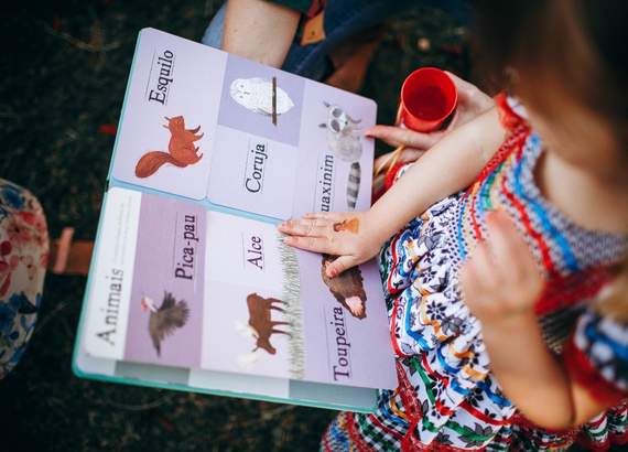 Criança vendo um livro com desenhos de animais e seus respectivos nomes ao lado. - Como ensinar a ler 8 dicas fáceis e práticas 