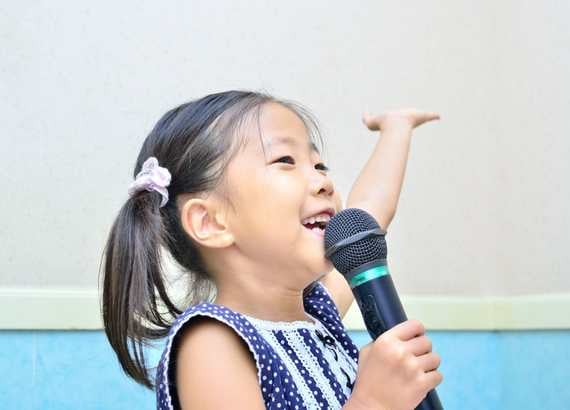 Menina feliz com microfone à mão cantando. Linguagens artísticas o que e quais são as linguagens da arte.