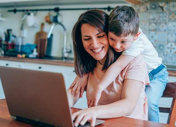 Crianças em casa: 10 dicas úteis para o home office e as férias. Criança sobre o ombro da mãe enquanto está trabalhando no computador.