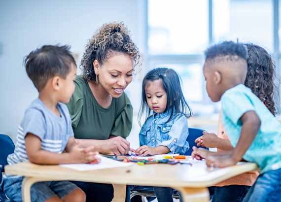 15 dicas para ajudar seus filhos durante a adaptação escolar. Professora fazendo atividade com alunos na creche.
