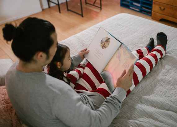Como escolher um método de ensino para o meu filho? Pai contando história para a sua filha, ambos sentados olhando para o livro.