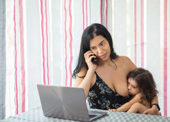 Amamentação: Mulher amamentando criança de mais de 2 anos. Ela está falando ao telefone e também trabalhando no computador.