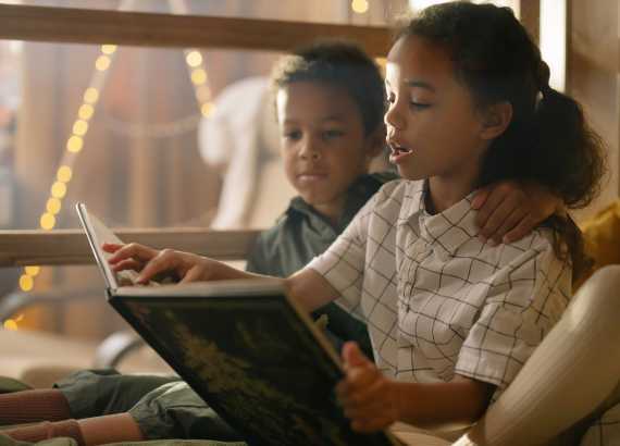 Protagonismo preto na literatura: entenda a importância de apresentar livros com diversidade para as crianças desde cedo
Duas crianças lendo um livro, o menino abraçado à menina que conta a história.