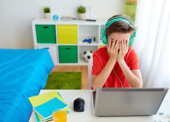 Jogos online e crianças: os perigos e cuidados nesse ambiente
Menino em notebook com mão no rosto chorando.