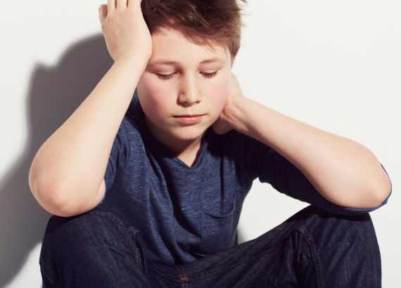 O que é a depressão infantil?
Criança sentada com mão na cabeça, expressão de angústia