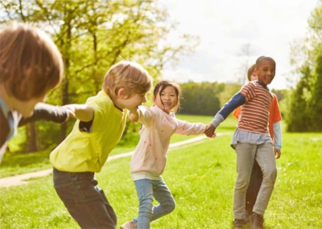 Foto de crianças brincando de mãos dadas num jardim ao ar livre.